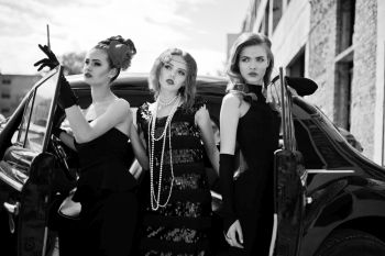 three ladies displaying flapper fashion, with a black car behind them